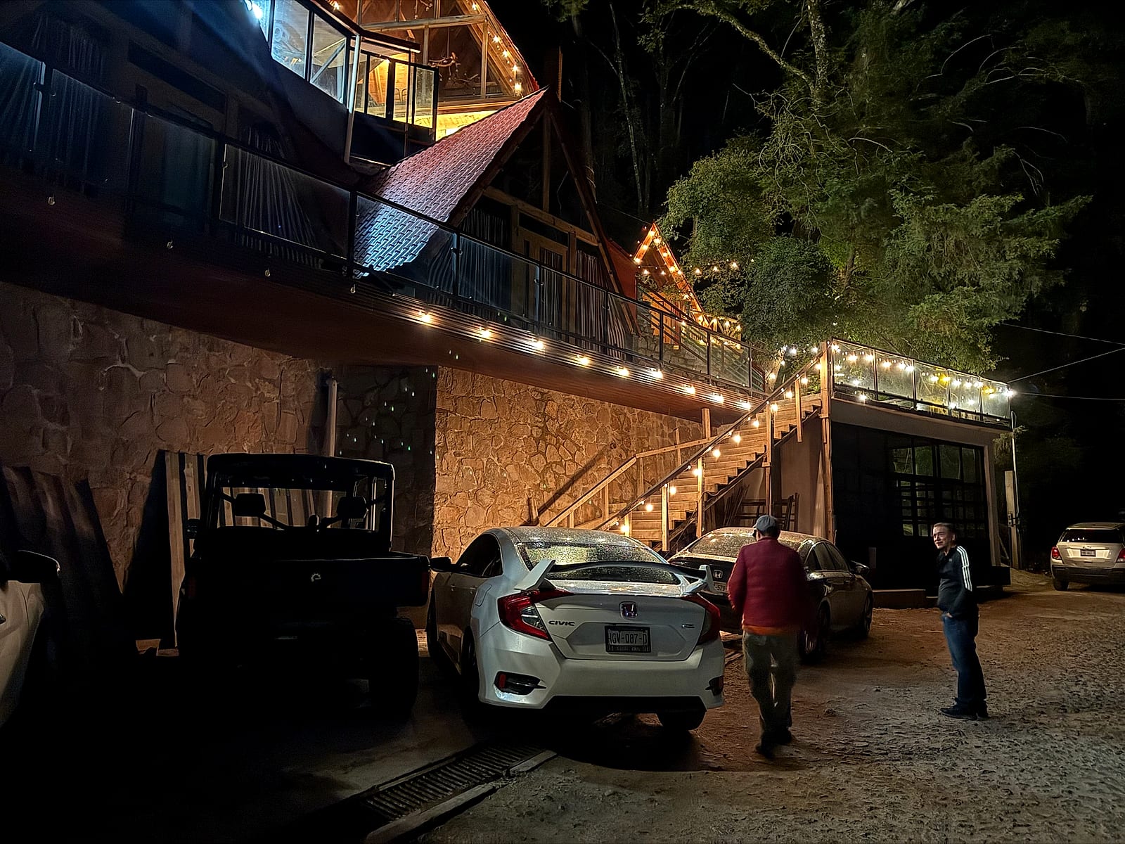 Las cabañas de noche con luces cálidas colgantes y los vehículos de aventura listos.