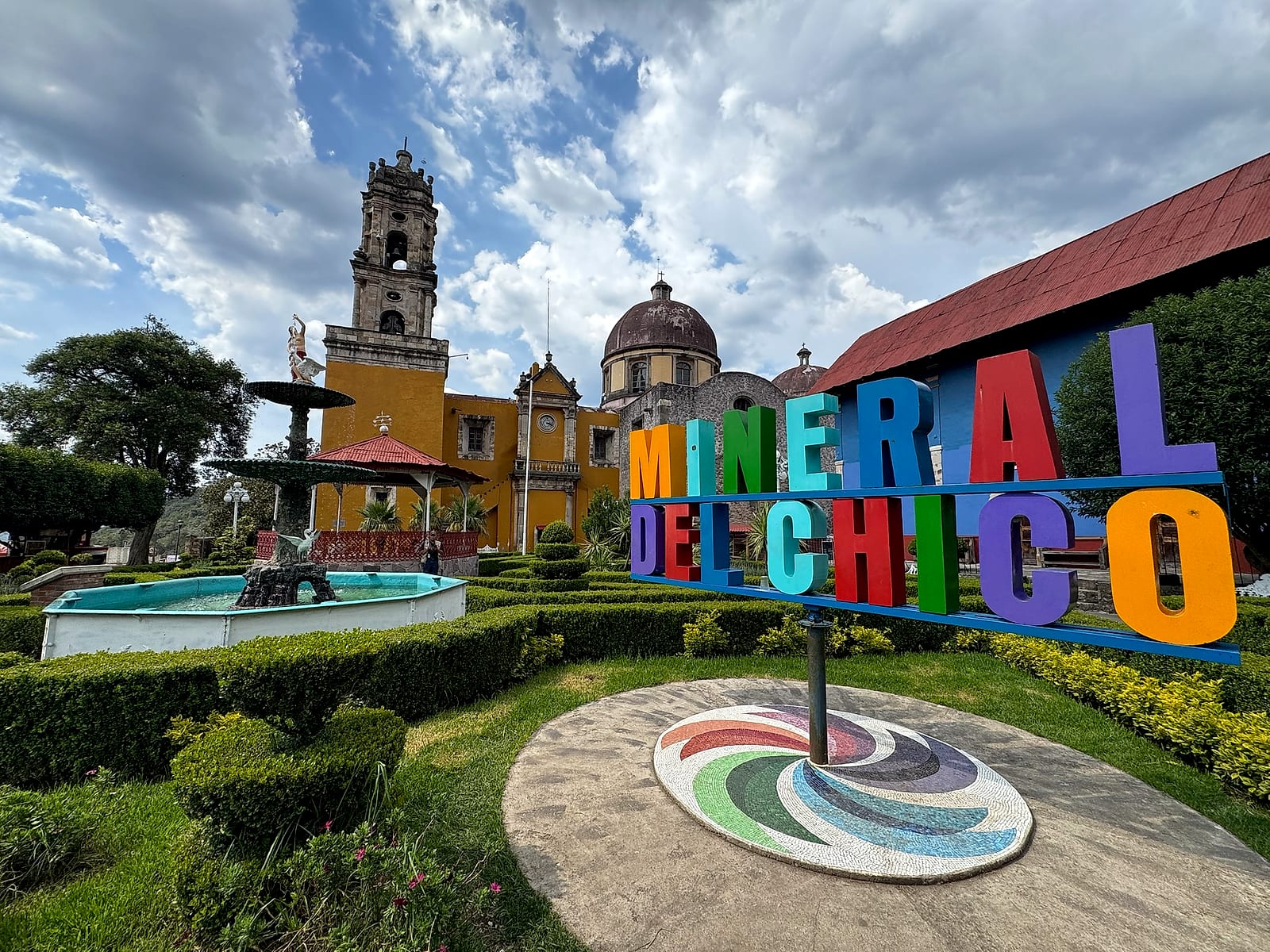 La parroquia amarilla y la fuente del jardín principal de Mineral del Chico bajo el sol.